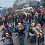 Fasnetsgruppe aus Erwachsenen und Kindern in traditionellen Häsern zieht während eines winterlichen Umzugs durch eine belebte Straße.