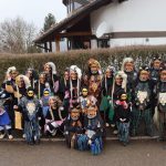 Gruppe aus Erwachsenen und Kindern in traditionellen Fasnetshäsern posiert für ein gemeinsames Foto vor einer Wohnsiedlung.