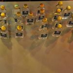 Mehrere Reihen kleiner Flaschen mit gelben Deckeln stehen geordnet auf einer beleuchteten Theke.