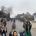 Fasnetsgruppe aus Erwachsenen und Kindern in traditionellen Häsern läuft eine Wohnstraße entlang während eines winterlichen Umzugs.