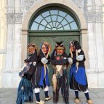 Vier Fasnetsfiguren in traditionellen Masken und farbigen Häsern stehen posierend vor einer großen grünen Holztür mit Rundbogen.