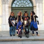 Gruppe von Fasnetsfiguren in traditionellen Masken und farbigen Häsern steht vor einer großen grünen Holztür mit Rundbogen.
