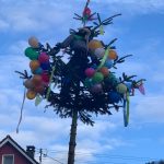 Geschmückter Narrenbaum mit bunter Dekoration, Luftballons und einer traditionellen Figur vor blauem Himmel.