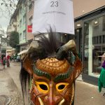 Fasnetsfigur mit Hörnern steht unter einem Schild mit der Aufschrift „23 – Narrenzunft Laimnau“ in einer Innenstadtstraße.