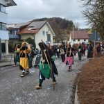 Traditionelle Fasnetsfiguren in farbigen Häs und mit Holzstäben laufen bei einem Straßenumzug durch ein Wohngebiet.