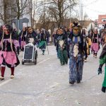 Gruppe traditioneller Fasnetsfiguren mit kunstvollen Masken und farbigen Häs läuft während eines Umzugs eine Straße entlang, begleitet von vielen Zuschauenden.