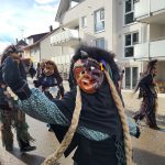 Fasnetsfiguren in traditionellen Kostümen und Holzmasken bei einem Straßenumzug in einem Wohngebiet.